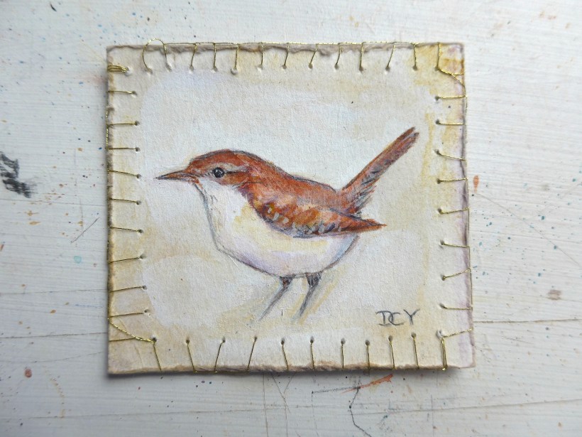 Painting showing painting of a wren on paper with gold thread decorating the edge by artist Diane Young